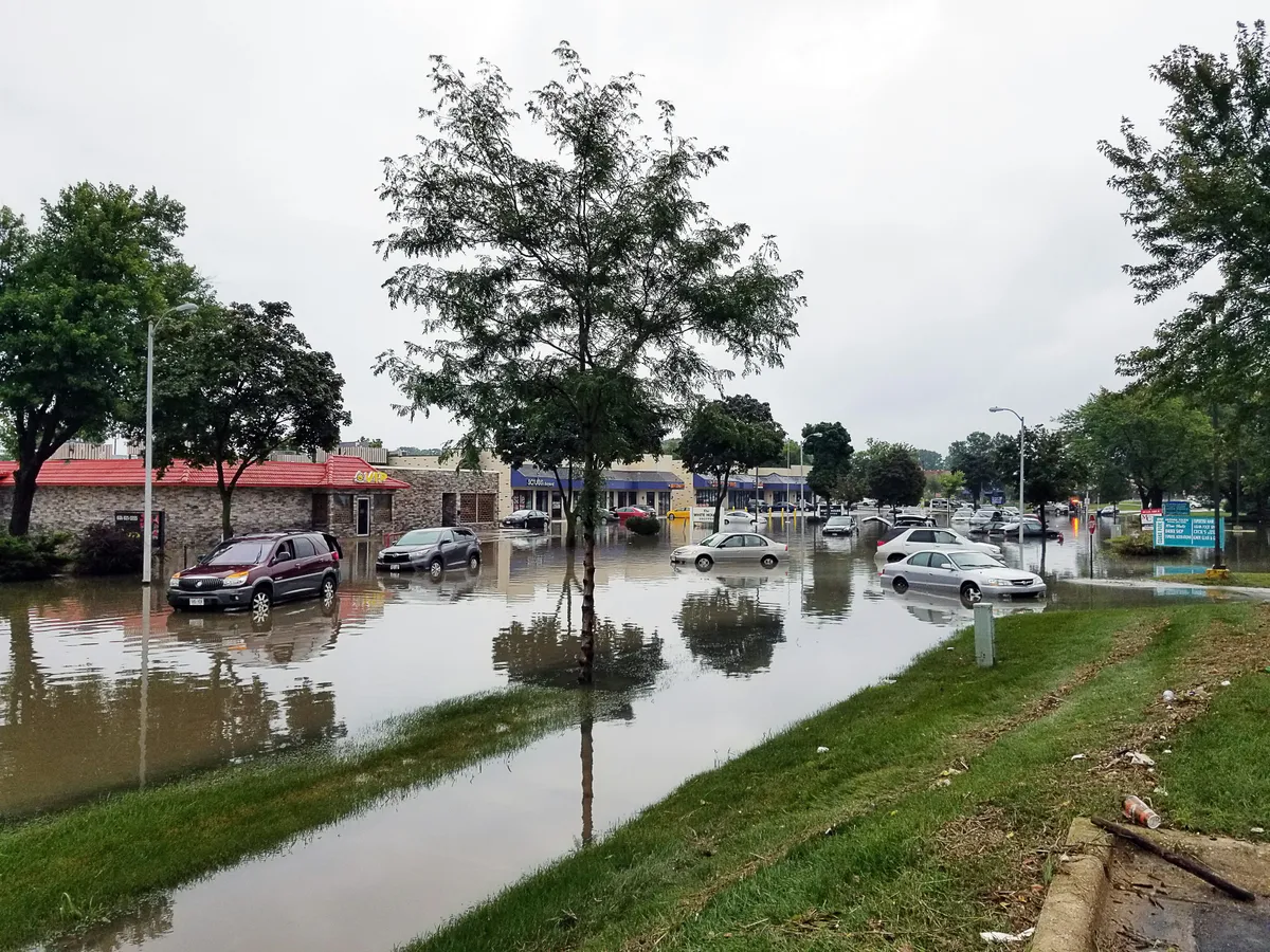 A flooded shopping center parking lot with partially submerged cars, indicating severe storm impact on retail businesses.