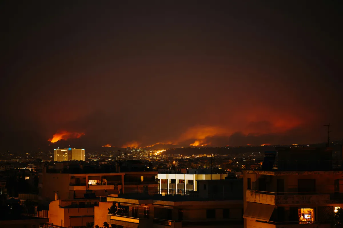 Urban landscape at nighttime with wildfires in the distance.